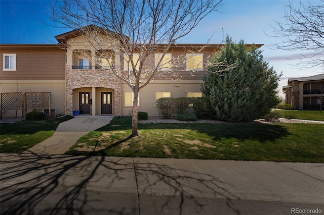 view of front facade with stucco siding, stone siding, and a front lawn