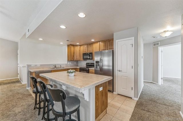 kitchen with visible vents, light carpet, a center island, a sink, and stainless steel appliances