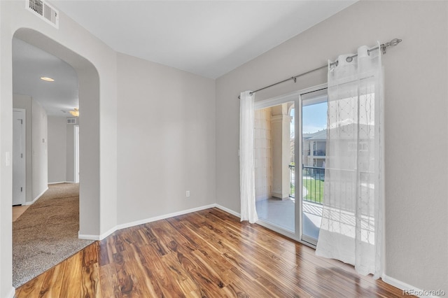 unfurnished room featuring arched walkways, baseboards, visible vents, and wood finished floors