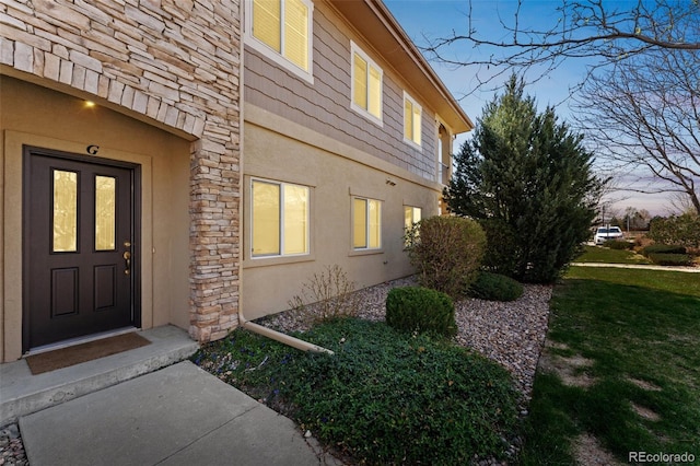 view of side of property featuring a yard, stone siding, and stucco siding