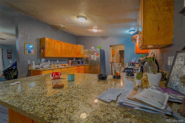 15682 Morris Ave, Fort Lupton, CO 80621 - kitchen with light stone counters, a textured ceiling, brown cabinetry, stainless steel appliances, and a textured wall