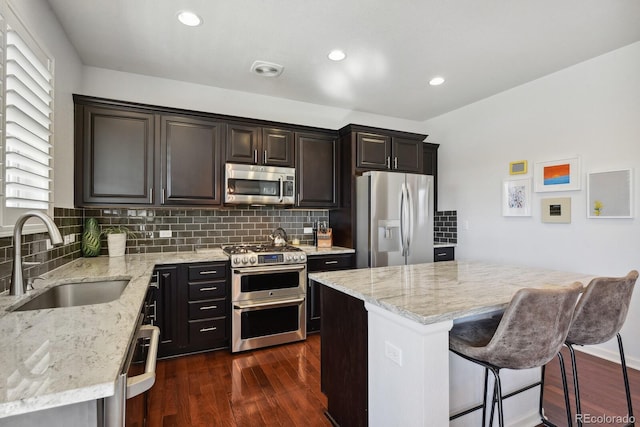 kitchen featuring appliances with stainless steel finishes, dark hardwood / wood-style floors, sink, a center island, and light stone countertops