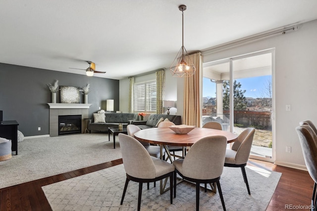 dining space featuring dark wood-type flooring, a tile fireplace, and ceiling fan