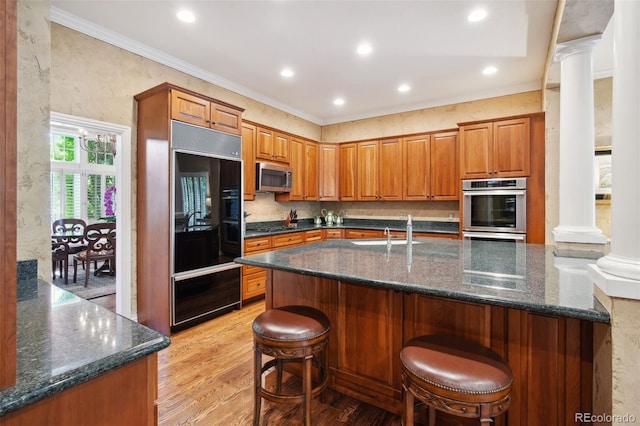 kitchen with a kitchen bar, ornate columns, stainless steel appliances, crown molding, and light hardwood / wood-style flooring