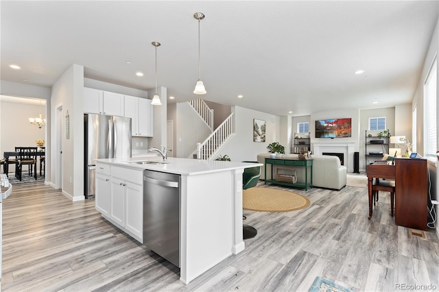 kitchen with hanging light fixtures, light hardwood / wood-style floors, white cabinetry, an island with sink, and stainless steel appliances