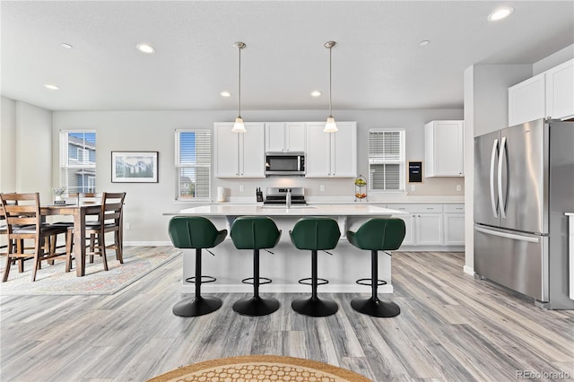 kitchen featuring white cabinets, stainless steel appliances, light hardwood / wood-style flooring, decorative light fixtures, and a kitchen island with sink