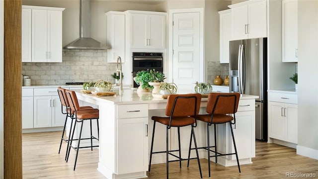 kitchen featuring stainless steel appliances, white cabinetry, wall chimney range hood, a breakfast bar area, and a kitchen island with sink