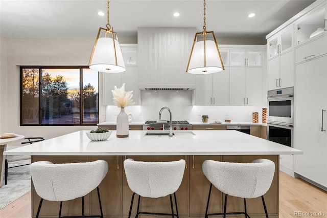 kitchen with pendant lighting, light hardwood / wood-style floors, white cabinetry, and an island with sink