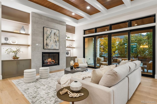 living room featuring built in features, beamed ceiling, a fireplace, wood ceiling, and light wood-type flooring