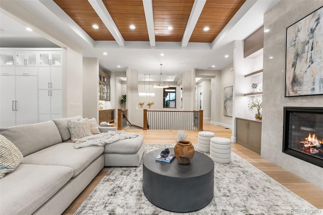 living room featuring beam ceiling, light wood-type flooring, wooden ceiling, and a tiled fireplace