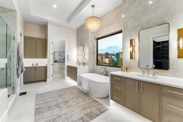 bathroom featuring plus walk in shower, tile patterned flooring, a notable chandelier, vanity, and tile walls