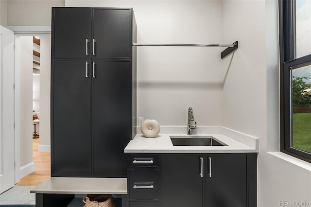 bar featuring light stone counters, light hardwood / wood-style flooring, and sink