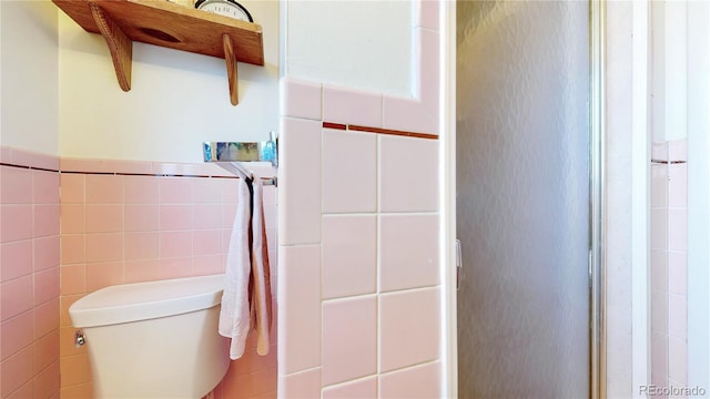 bathroom with toilet, a wainscoted wall, and tile walls