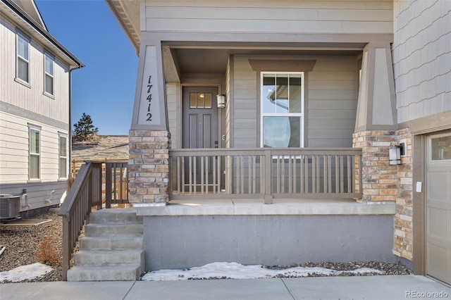 view of exterior entry with a garage, covered porch, and central air condition unit