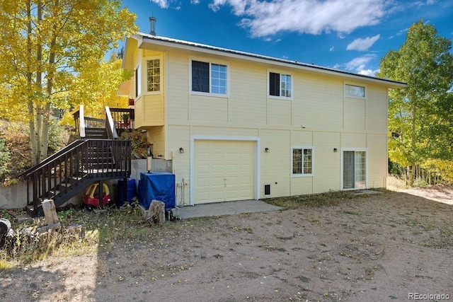 rear view of house featuring an attached garage, dirt driveway, and stairway