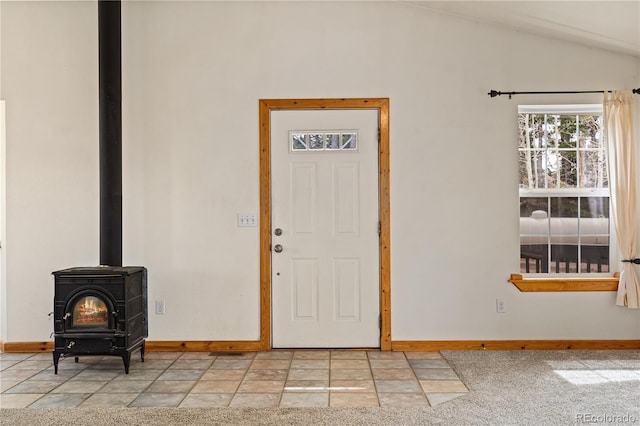 foyer featuring baseboards, a wood stove, stone tile floors, and lofted ceiling