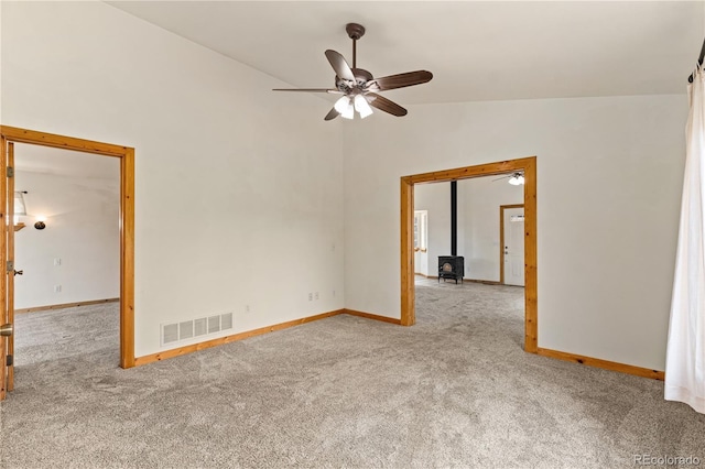 carpeted empty room featuring a ceiling fan, lofted ceiling, a wood stove, and baseboards