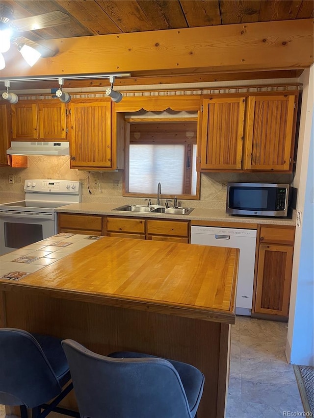 60 Pawnee Path, Lake George, CO 80827 - kitchen featuring white appliances, under cabinet range hood, tasteful backsplash, a breakfast bar area, and brown cabinetry