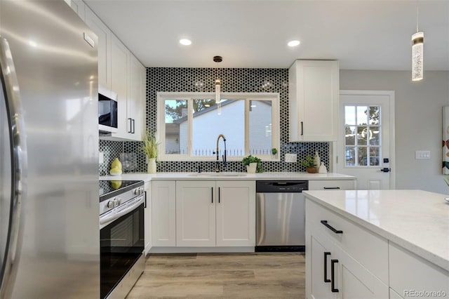 kitchen featuring pendant lighting, a sink, tasteful backsplash, white cabinetry, and stainless steel appliances