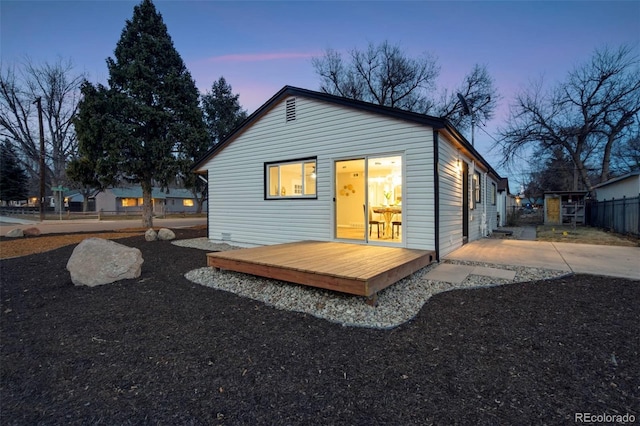 back of house at dusk featuring a deck and fence