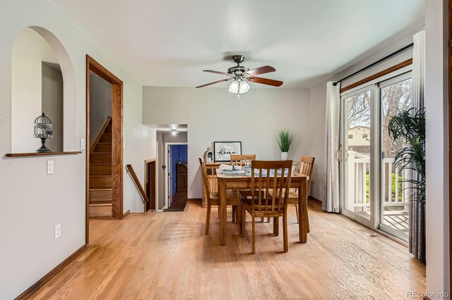 dining area with arched walkways, stairs, a ceiling fan, baseboards, and light wood-type flooring