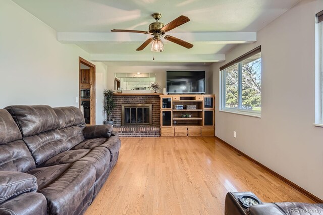 living room with a fireplace, a ceiling fan, beamed ceiling, and light wood-style floors