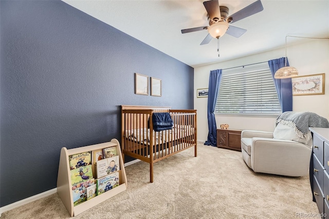 bedroom featuring light carpet, a nursery area, and ceiling fan