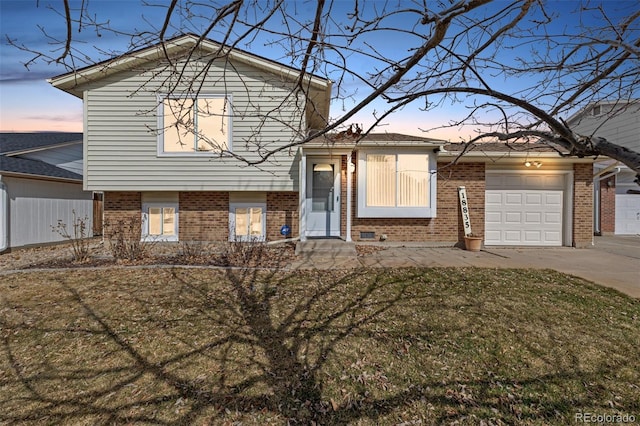 tri-level home featuring an attached garage, driveway, a front yard, and brick siding