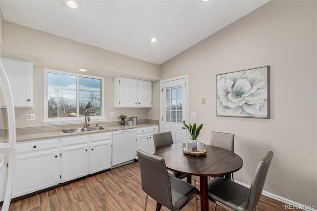 kitchen featuring dishwasher, vaulted ceiling, light countertops, white cabinetry, and a sink