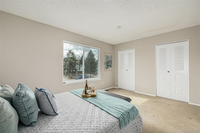 carpeted bedroom with baseboards, a textured ceiling, and multiple closets