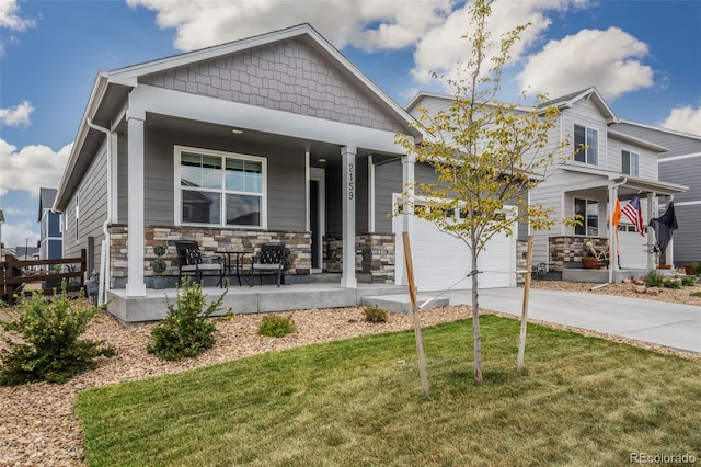 craftsman-style house with driveway, stone siding, an attached garage, covered porch, and a front lawn