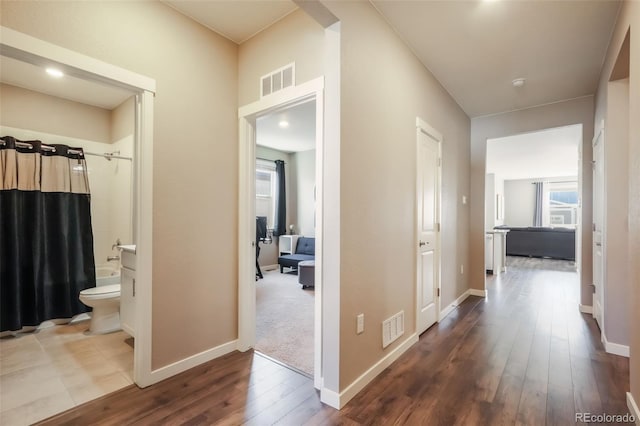 hallway featuring wood finished floors, visible vents, and baseboards