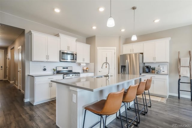 kitchen featuring appliances with stainless steel finishes, hanging light fixtures, a kitchen island with sink, light countertops, and white cabinetry