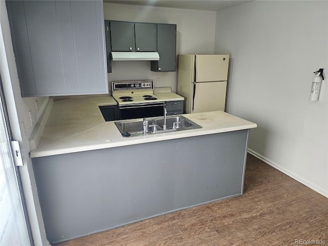 kitchen with under cabinet range hood, a peninsula, range with electric stovetop, light countertops, and freestanding refrigerator