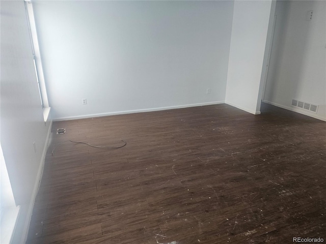 empty room featuring dark wood finished floors, visible vents, and baseboards