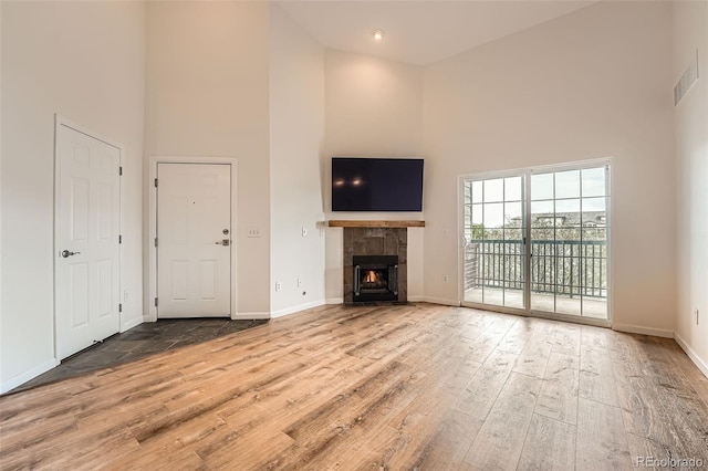 unfurnished living room featuring a towering ceiling, wood finished floors, baseboards, and a tile fireplace
