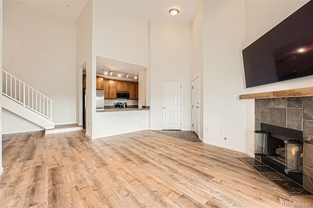 unfurnished living room with a high ceiling, track lighting, wood finished floors, baseboards, and a tile fireplace