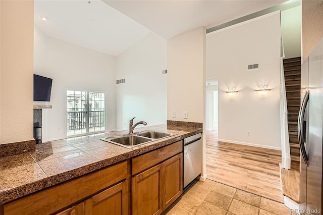 kitchen with a sink, appliances with stainless steel finishes, tile countertops, brown cabinetry, and high vaulted ceiling