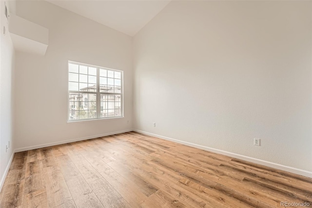 empty room featuring light wood finished floors, baseboards, and high vaulted ceiling