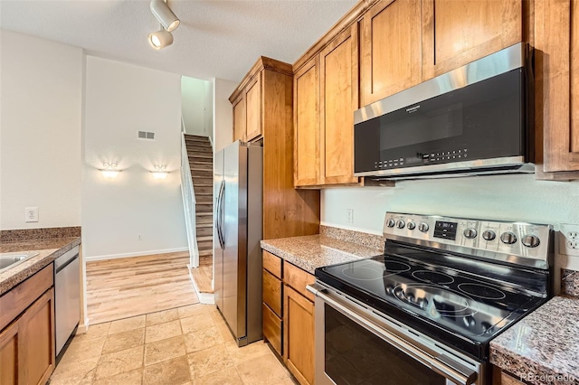 kitchen with stainless steel appliances, brown cabinets, light stone finish floors, and rail lighting