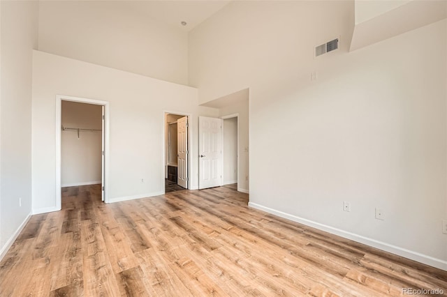 unfurnished bedroom featuring a spacious closet, light wood-style floors, a towering ceiling, baseboards, and a closet