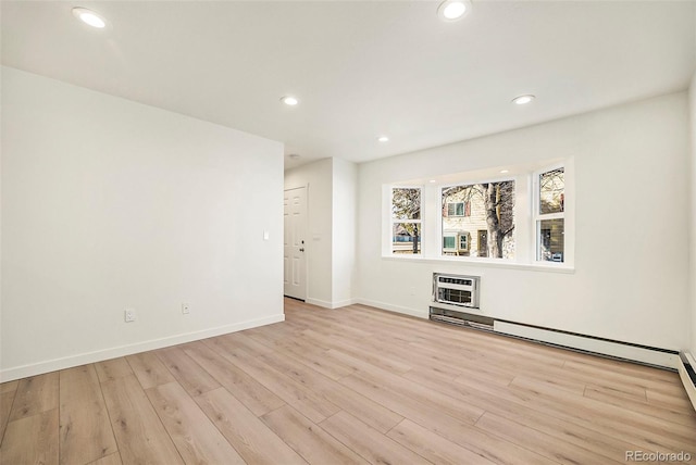 unfurnished room with heating unit, a baseboard radiator, light hardwood / wood-style flooring, and an AC wall unit