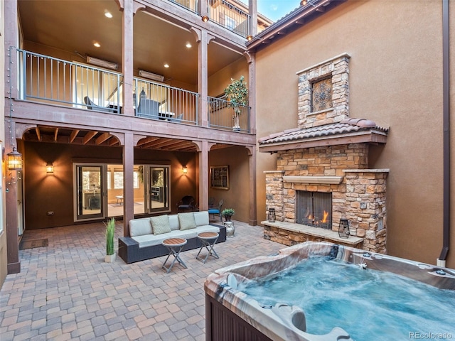 view of patio / terrace with a hot tub, a balcony, and an outdoor living space with a fireplace