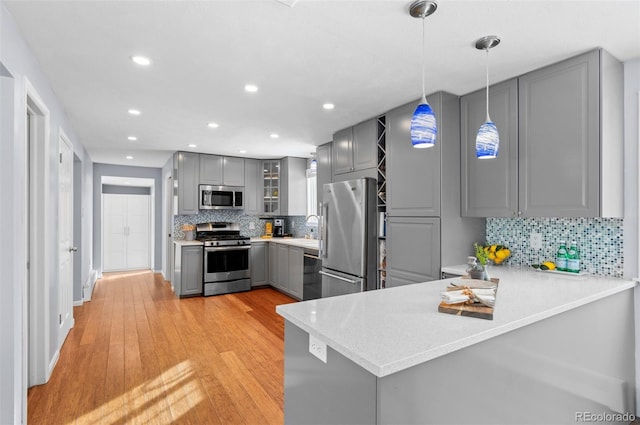 kitchen with pendant lighting, appliances with stainless steel finishes, kitchen peninsula, light wood-type flooring, and gray cabinetry