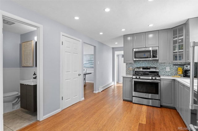 kitchen with gray cabinets, light hardwood / wood-style floors, tasteful backsplash, and stainless steel appliances