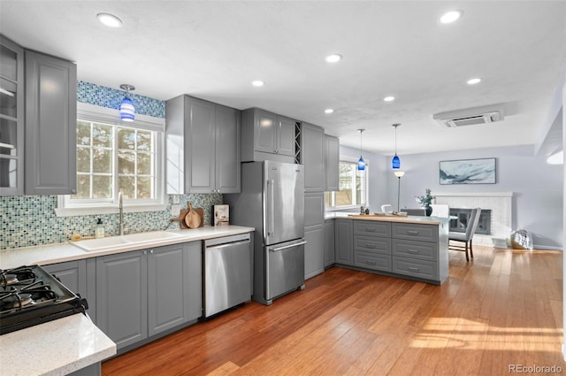 kitchen with pendant lighting, appliances with stainless steel finishes, sink, backsplash, and gray cabinets