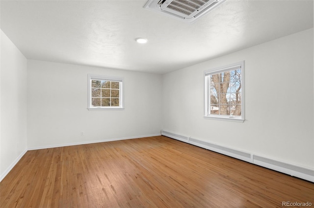 unfurnished room with light wood-type flooring, a healthy amount of sunlight, and a baseboard heating unit