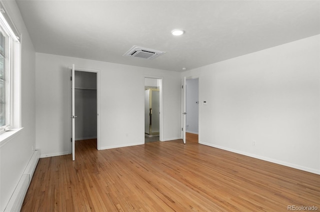 unfurnished bedroom featuring light wood-type flooring, a closet, a baseboard heating unit, and a spacious closet