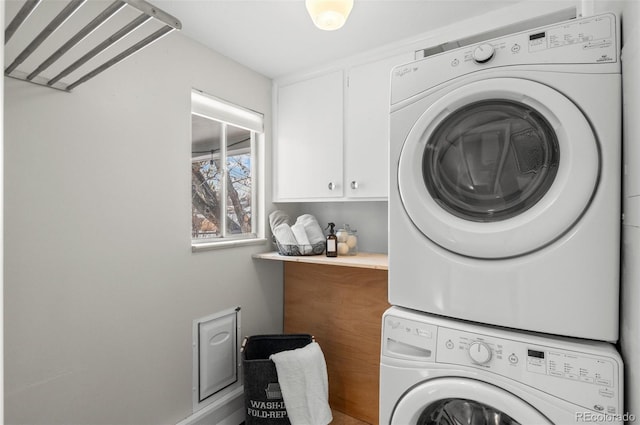 laundry area featuring stacked washer / drying machine and cabinets