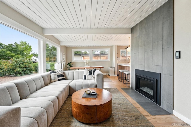 1440 S Clermont St, Denver, CO 80222 - living area featuring light wood-style floors, a tiled fireplace, wooden ceiling with exposed beams, and baseboards